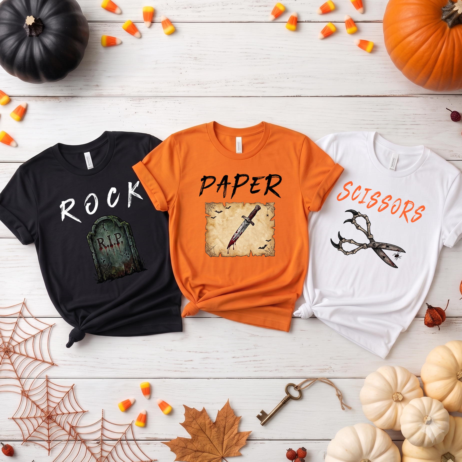 Three Halloween-themed t-shirts on a wooden surface with pumpkins and leaves.