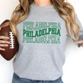 Person wearing a gray sweatshirt with 'PHILADELPHIA' printed three times in green, holding a football.