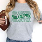 Person wearing a gray sweatshirt with 'PHILADELPHIA' printed three times in green, holding a football.