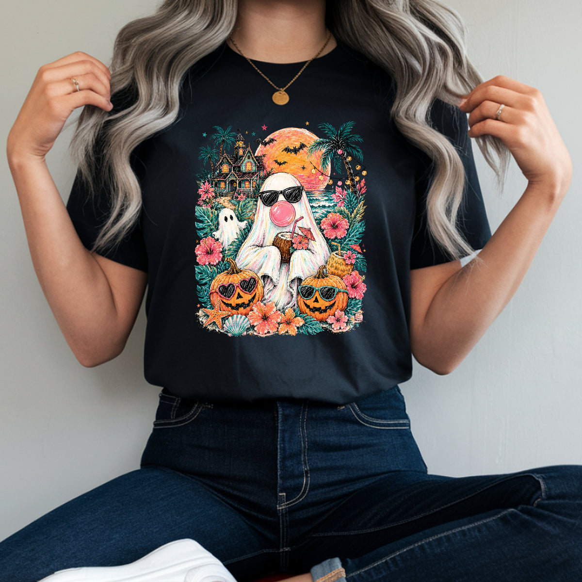 A woman wearing a black graphic t-shirt with a Halloween-themed print of a stormtrooper surrounded by pumpkins, ghosts, and flowers. She is sitting cross-legged on a red stool, wearing dark blue jeans and white sneakers against a plain light gray wall.