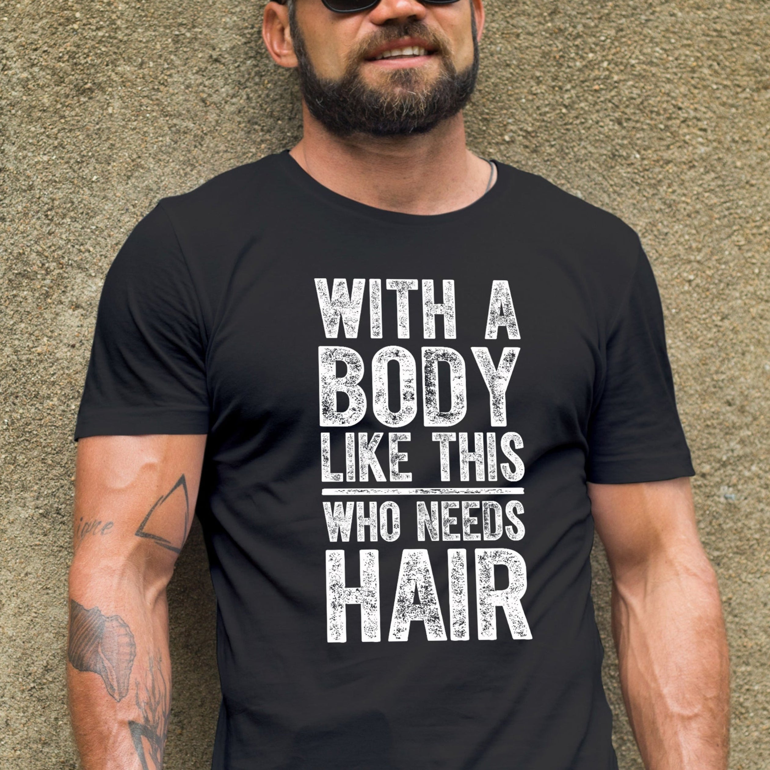 Man wearing a black t-shirt with text and sunglasses, standing against a textured wall.