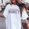Person wearing a white oversized t-shirt with 'American Honey' text outdoors.