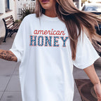 Person wearing a white oversized t-shirt with 'American Honey' text outdoors.