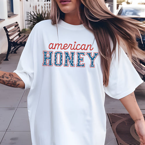 Person wearing a white oversized t-shirt with 'American Honey' text outdoors.