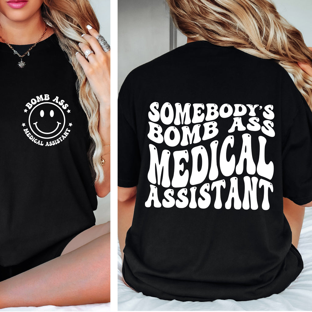 Black t-shirt with 'Bomb Ass Medical Assistant' text and smiley face design on a person.
