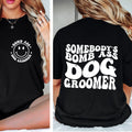 Black t-shirt with 'Somebody's Bomb Ass Dog Groomer' text and smiley face design on a person.