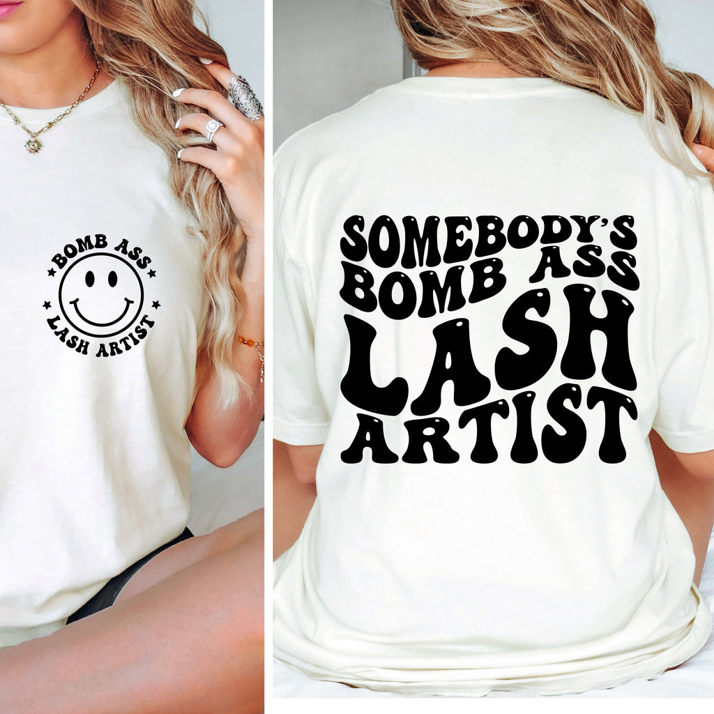 White t-shirt with 'Bomb Ass Lash Artist' text and smiley face on front, worn by a person.