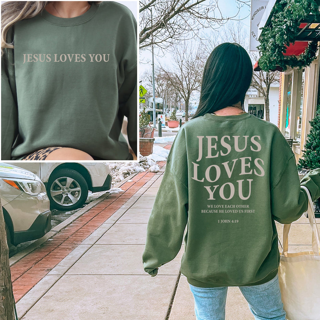 Person wearing a green sweatshirt with 'Jesus Loves You' text, walking on a sidewalk.
