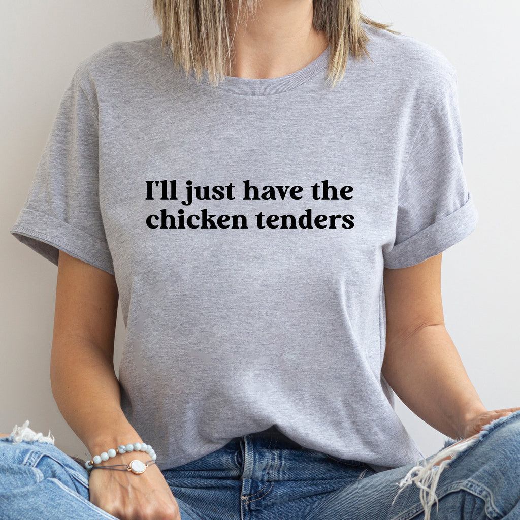 Person wearing a gray t-shirt with text 'I'll just have the chicken tenders' on a plain background