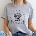 Person wearing a gray t-shirt with a cow graphic and text.