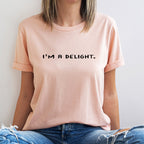 Person wearing a light pink t-shirt with 'I'm a Delight' text, sitting against a white background.