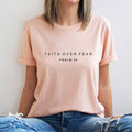 Person wearing a light pink t-shirt with text sitting against a plain background