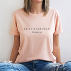 Person wearing a light pink t-shirt with text sitting against a plain background
