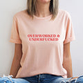 Person wearing a pink t-shirt with 'OVERWORKED & UNDERFUCKED' text.