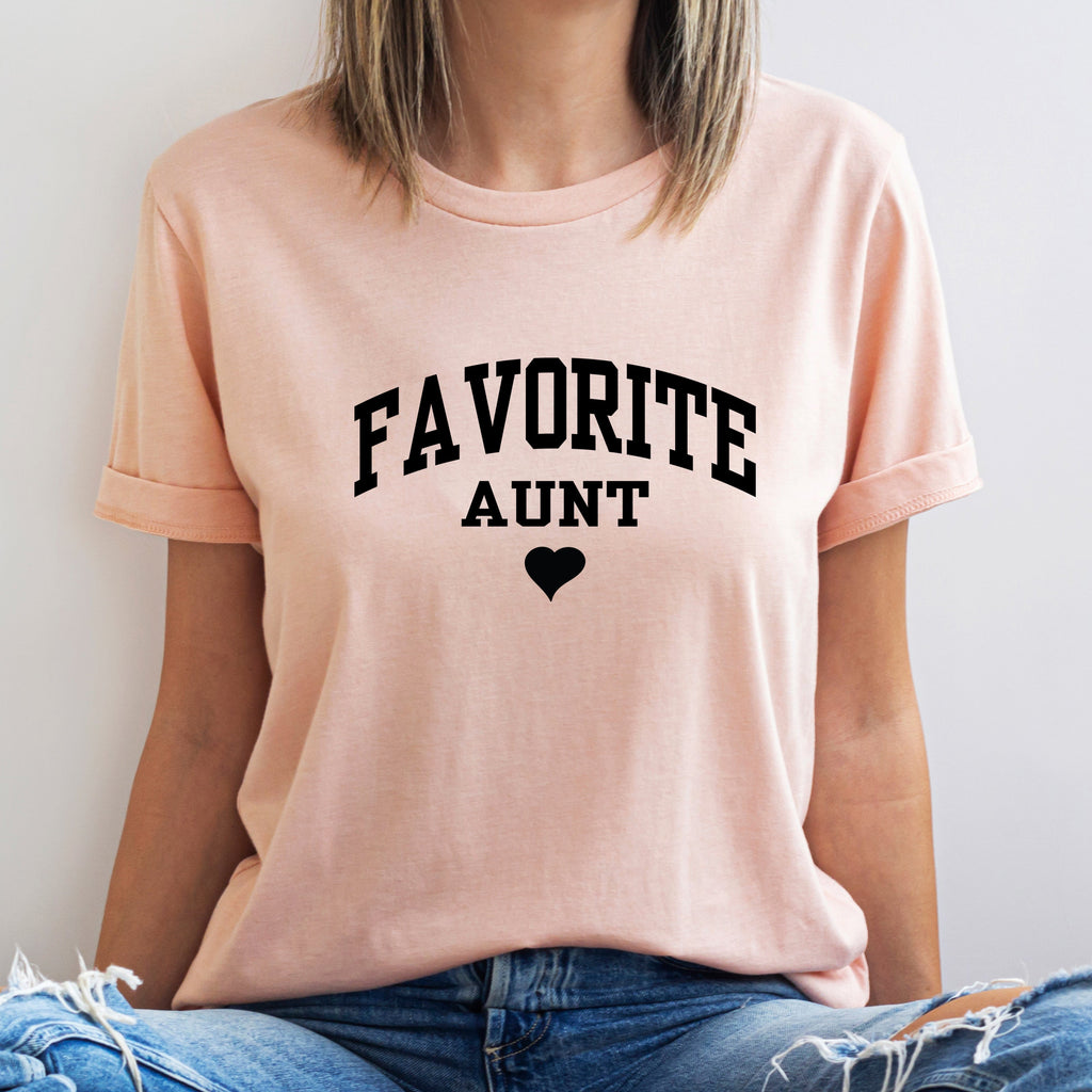 Person wearing a pink t-shirt with 'FAVORITE AUNT' text and a heart symbol on a light background
