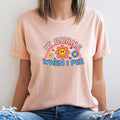 Person wearing a light pink t-shirt with colorful graphic and text against a plain background
