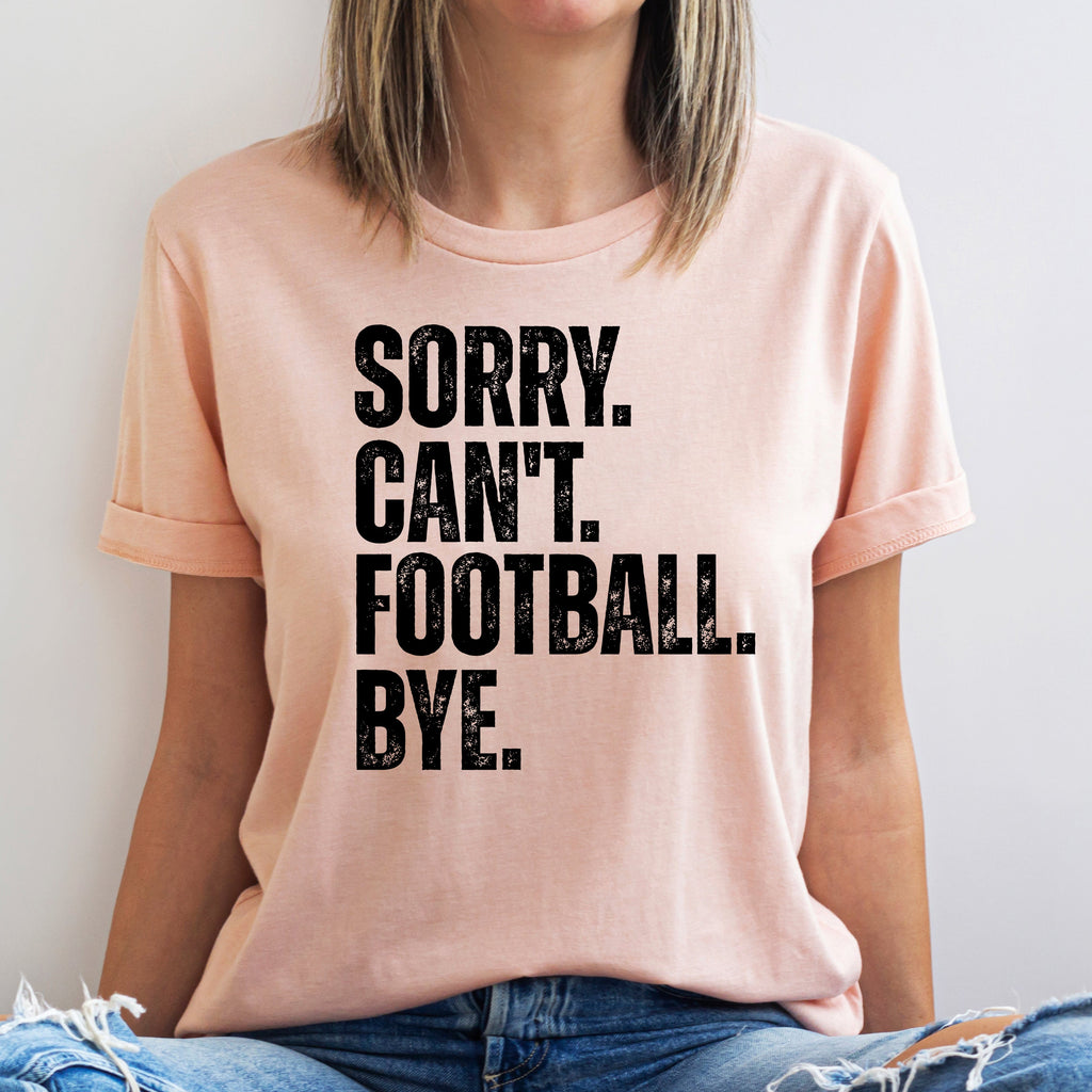 Person wearing a pink t-shirt with 'SORRY. CAN'T. FOOTBALL. BYE.' text on a plain background