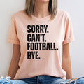 Person wearing a pink t-shirt with 'SORRY. CAN'T. FOOTBALL. BYE.' text on a plain background