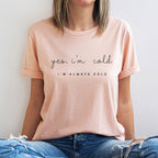 Person wearing a light pink t-shirt with text sitting against a plain background