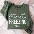 Green sweatshirt with 'Literally Freezing Me 24/7' text on a wooden floor.