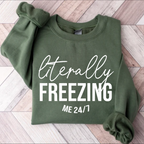 Green sweatshirt with 'Literally Freezing Me 24/7' text on a wooden floor.
