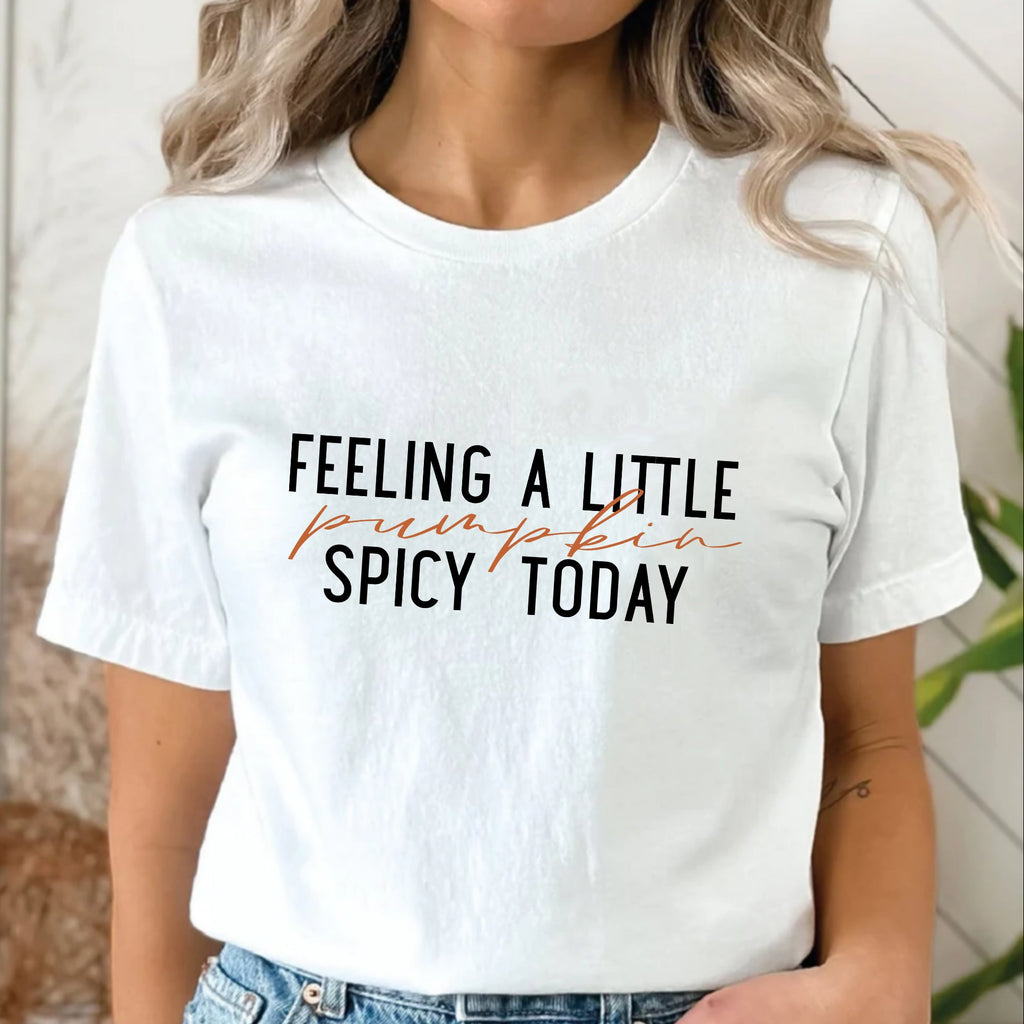 Person wearing a white t-shirt with text 'Feeling a little pumpkin spicy today' in an indoor setting.