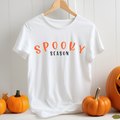 White t-shirt with 'Spooky Season' text on a hanger with pumpkins around