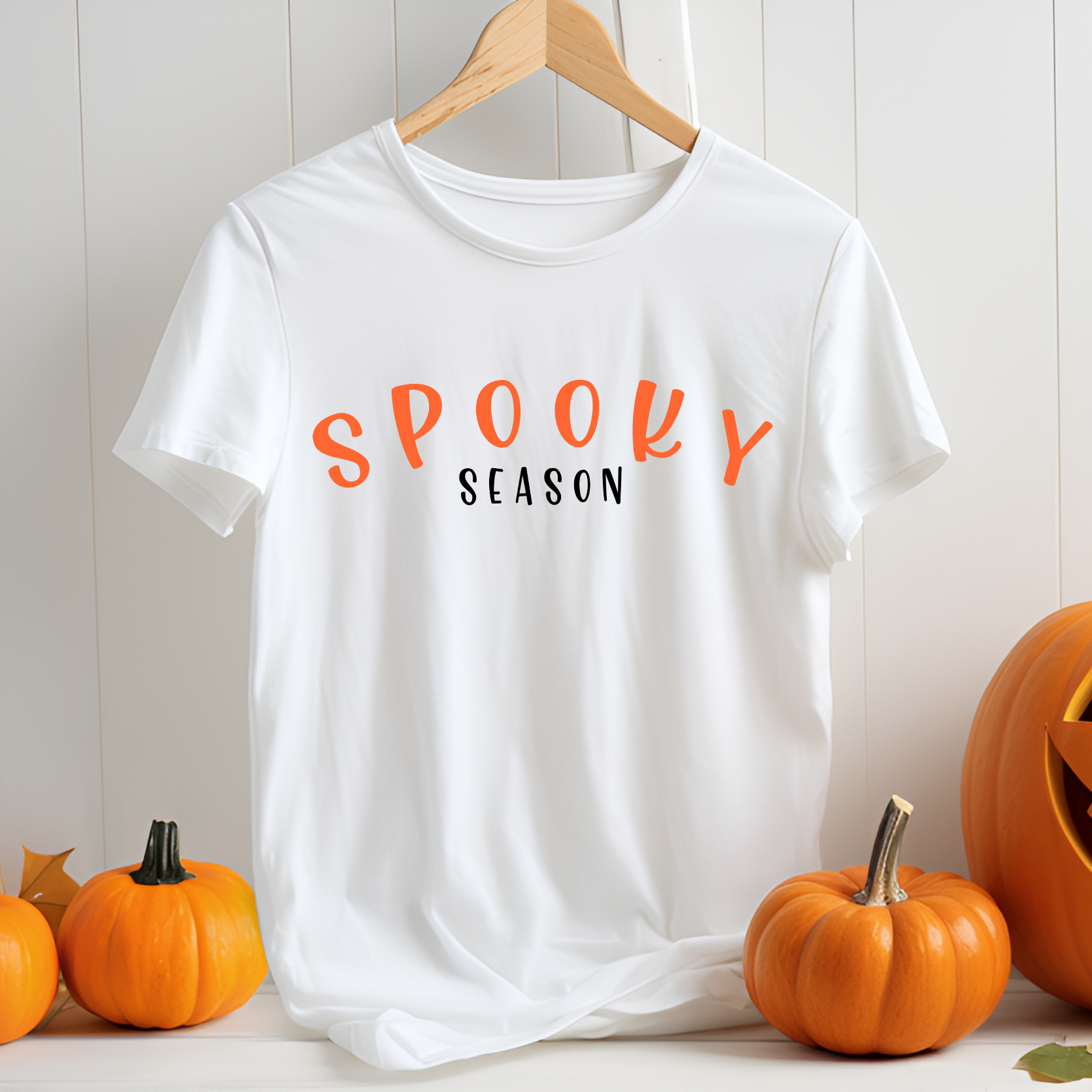 White t-shirt with 'Spooky Season' text on a hanger with pumpkins around