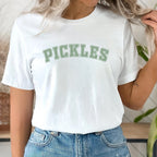 Person wearing a white t-shirt with 'PICKLES' text in a casual setting